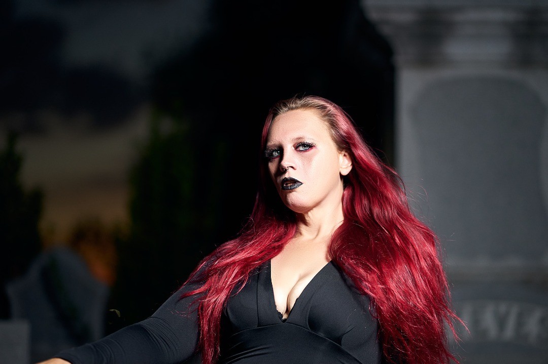 Starrgazzee with red hair and black clothing against a dark stone backdrop