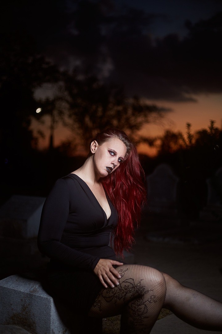 Starrgazzee seated in a black outfit with a warm evening sky behind her