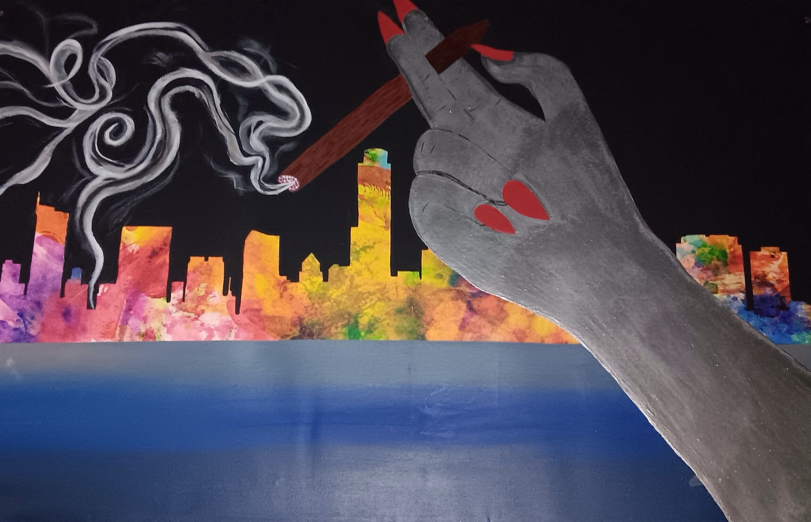 A hand holding a cigarette above a colorful skyline reflected in water