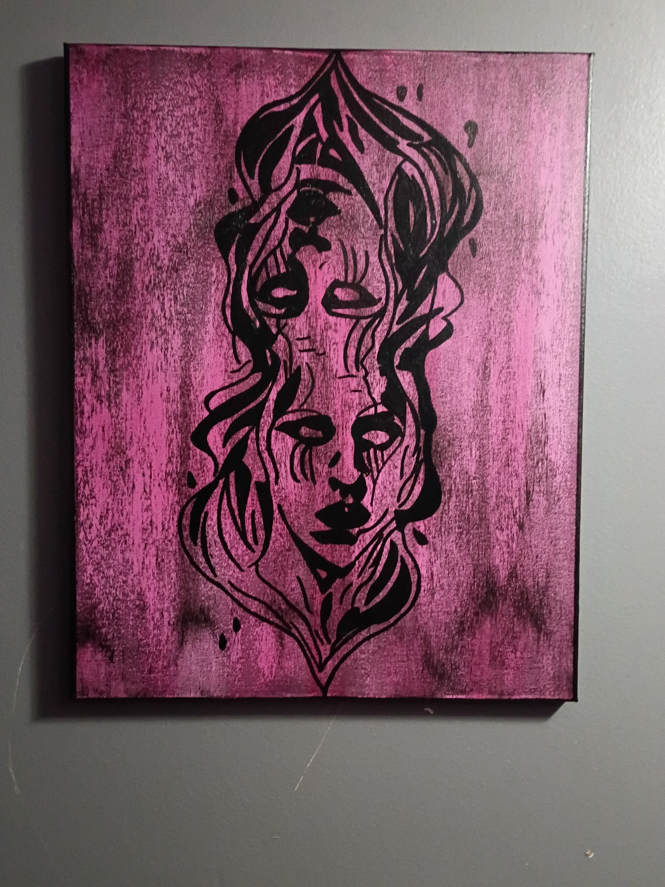 Two opposing faces painted in black on a pink canvas. Shown in a room.