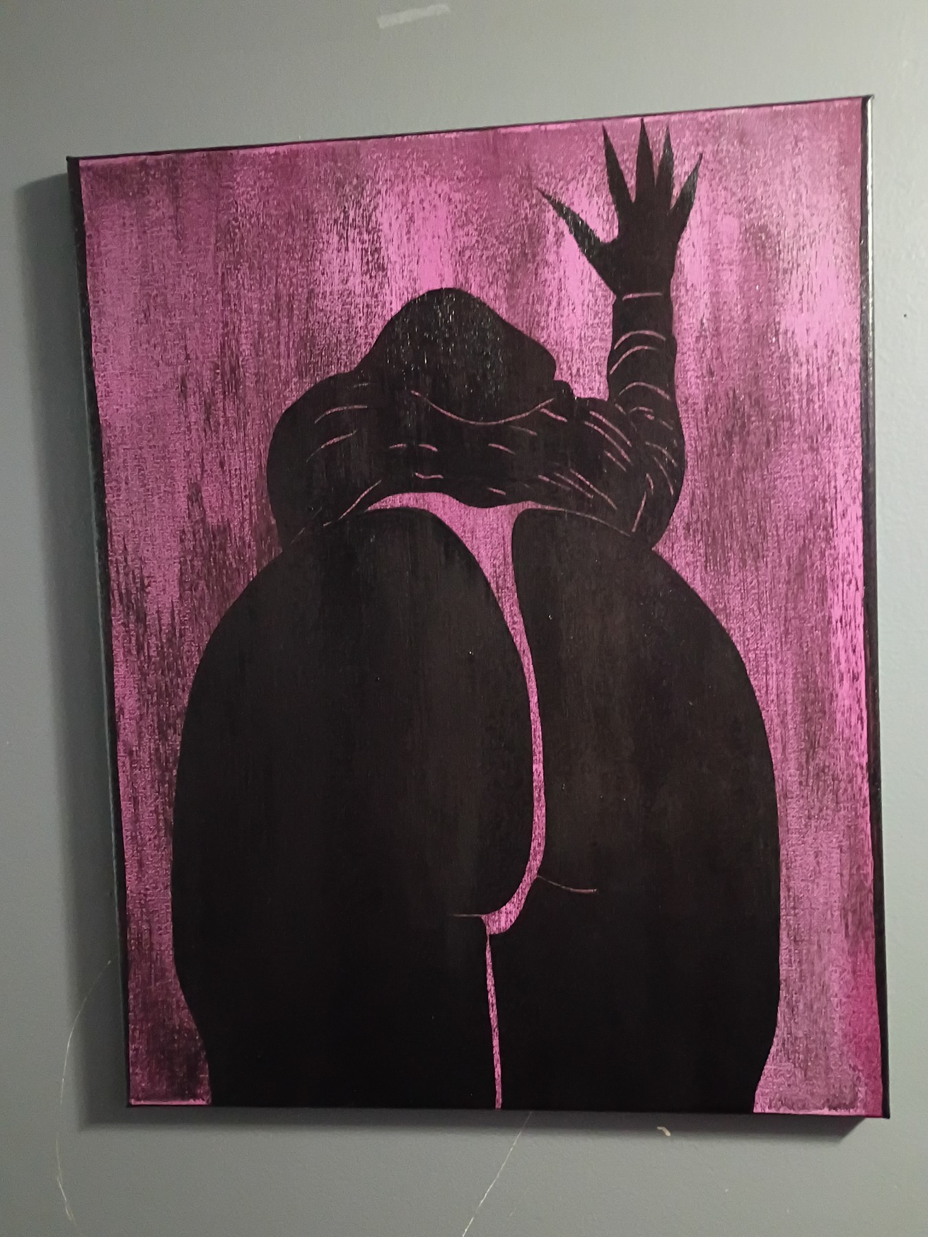 A black seated figure with a raised hand on a pink canvas. Shown in a room.
