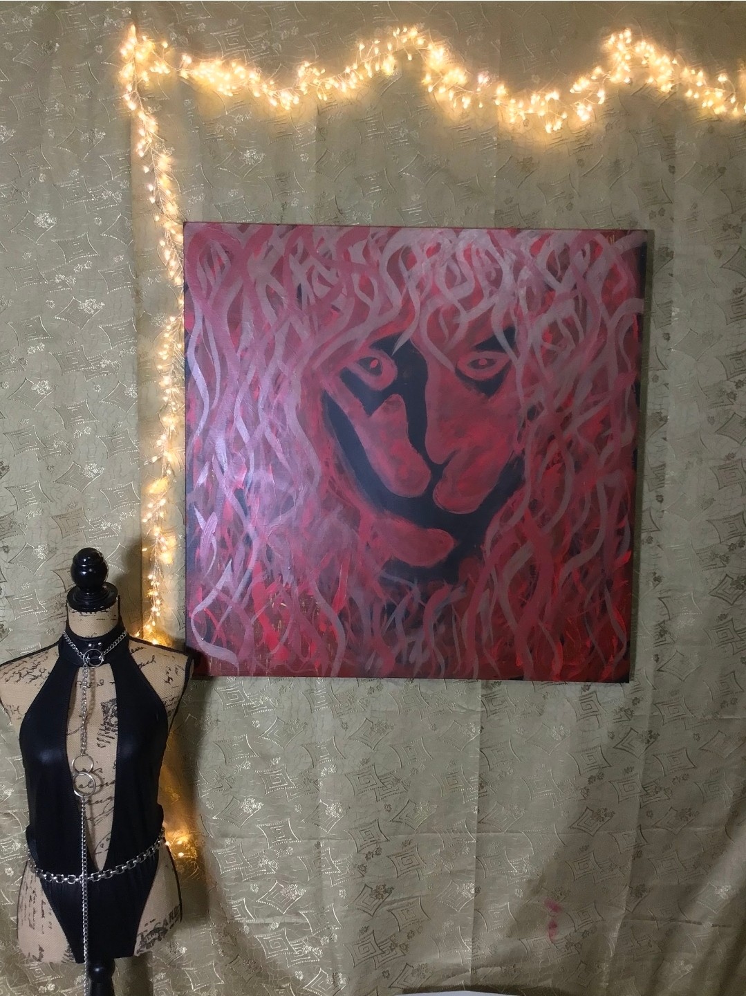 A lion face in black, red and pink beneath a flowing painted mane. Shown in a room.