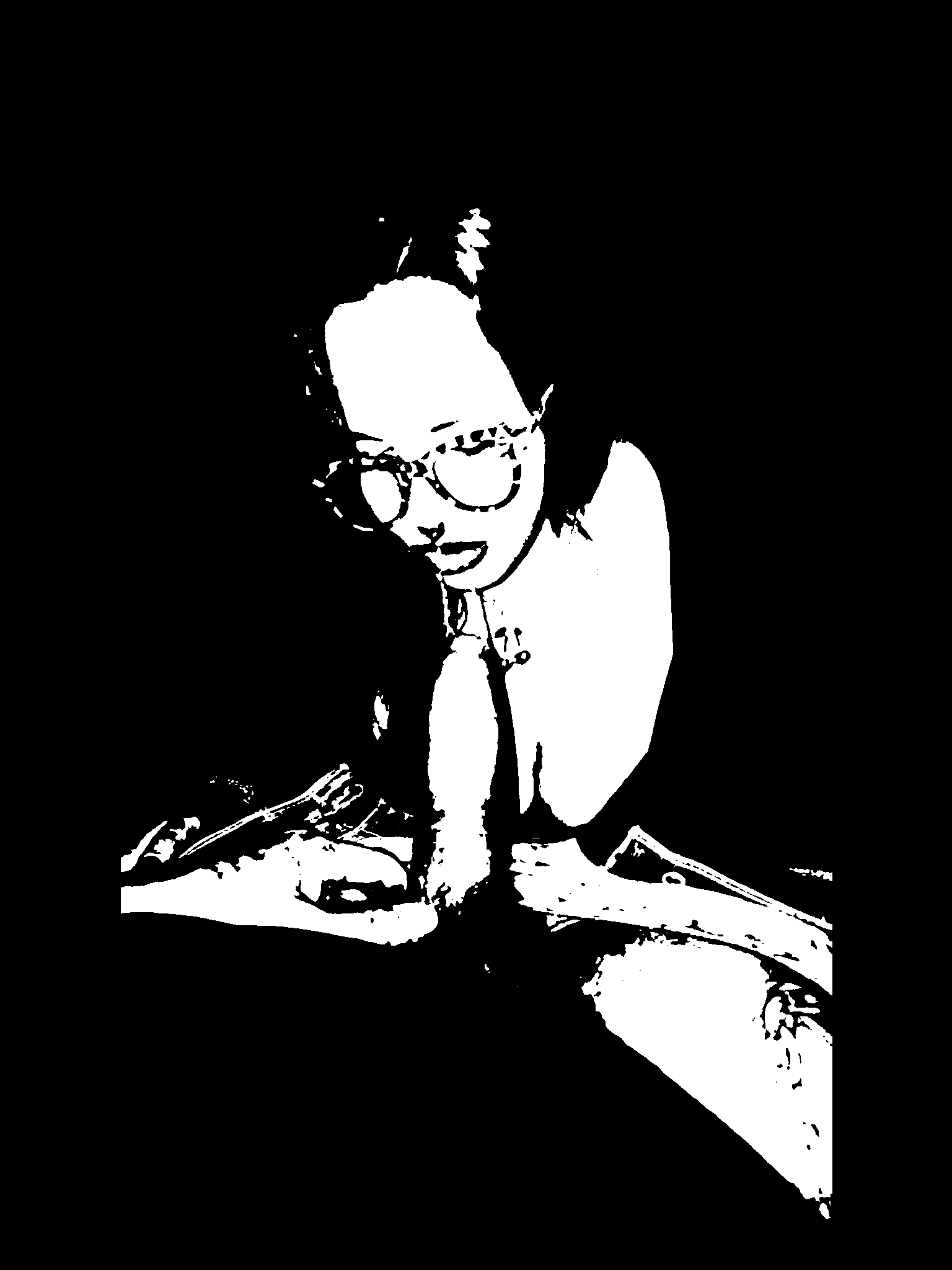 Black-and-white portrait of a figure leaning forward in clear-framed glasses with both hands resting in front