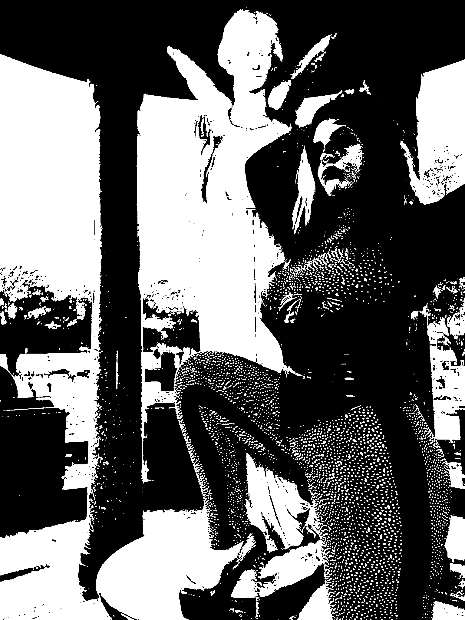 Black-and-white portrait of a seated figure with one arm raised beside her head and a winged statue behind her